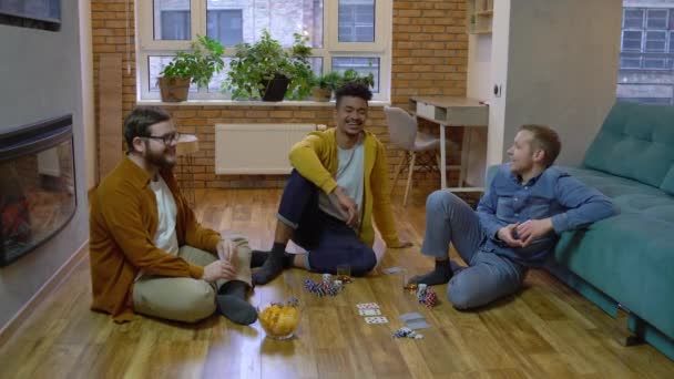 Amigos masculinos multiétnicos hablando y jugando al póquer en casa, divirtiéndose juntos — Vídeo de stock