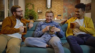 Erkek arkadaşlar bira içiyor, kanepede konuşuyor, ev partisinde birlikte eğleniyorlar.