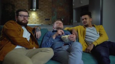 Üç sıkılmış adam kanepede oturup patlamış mısır yiyor.