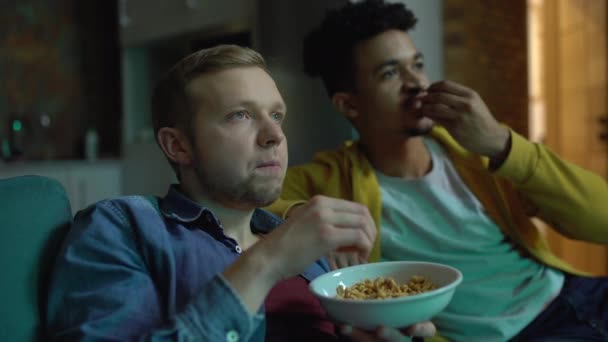 2人の男性の友人はテレビでサッカーの試合を見て、ゴールを祝い、軽食を噛む — ストック動画