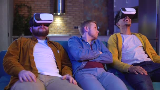 Молодой человек сидит скучно между двумя друзьями в VR гарнитуры, современные технологии — стоковое видео
