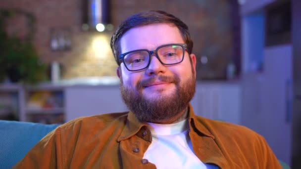 Γενειοφόρος νεαρός άνδρας με γυαλιά χαμογελά φιλικά στην κάμερα, ευτυχισμένος με τη ζωή της νεολαίας — Αρχείο Βίντεο
