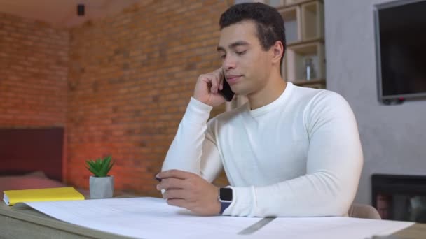 Man freelancer praten over de telefoon, werken aan architectonische blauwdruk thuis — Stockvideo