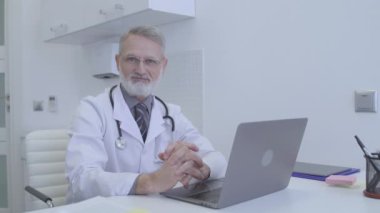 Arkadaş canlısı terapist masada oturuyor, kameraya gülümsüyor, sağlık hizmetleri...