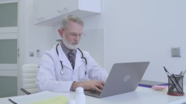 Dizüstü bilgisayarda çalışan, tıbbi sonuç yazan, sağlık hizmetleriyle meşgul bir kıdemli doktor.