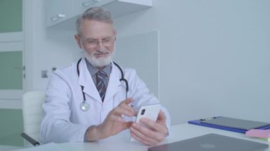 Kıdemli doktor tıbbi test sonuçlarını ve modern teknolojiyi görmek için akıllı telefonu kullanıyor.
