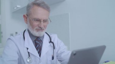 Tablet üzerinde çalışan, hastaların tıbbi kayıtlarını okuyan meşgul bir tıp doktoru.