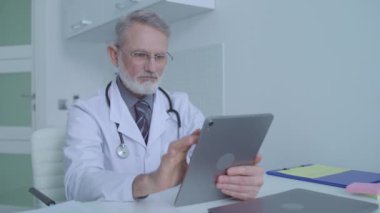 Tıbbi pratisyen, tablet üzerindeki bilgileri izliyor, hastaların test sonuçlarını kontrol ediyor