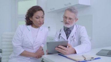 Tablete bakan erkek ve kadın doktorlar, hastaların iyileşme sürecini tartışıyor.