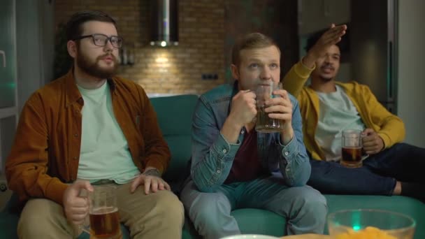 Zdenerwowani młodzi mężczyźni oglądający futbol, smutni z powodu przegranej gry, pijący piwo — Wideo stockowe