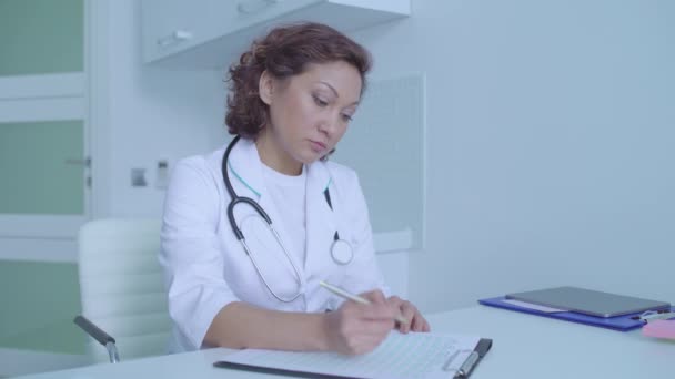 Family doctor writing in medical insurance document consulting patient in clinic — Stock Video