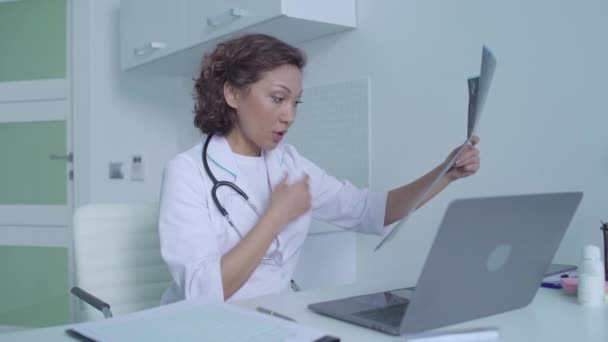 Грустная онколог смотрит на изображение опухоли, печатает на ноутбуке, плохой диагноз — стоковое видео