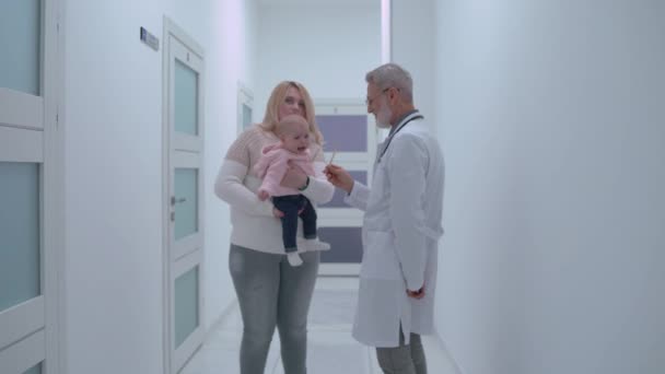 Jonge moeder houdt baby en praten met huisarts op kliniek hal, geneeskunde — Stockvideo
