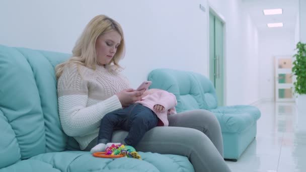 Hastanede rahat bir koltukta oturan genç bir kadın, kollarında uyuyan bir bebek. — Stok video