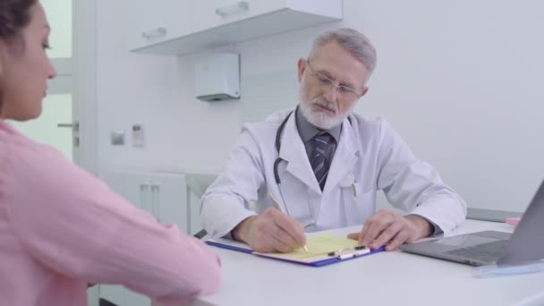 Terapeuta profesional que escribe prescripción, sentado en la mesa, servicio médico — Vídeos de Stock