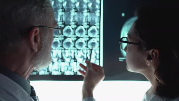 Dwóch lekarzy w okularach omawia diagnozę, analizując obraz tomograficzny — Wideo stockowe