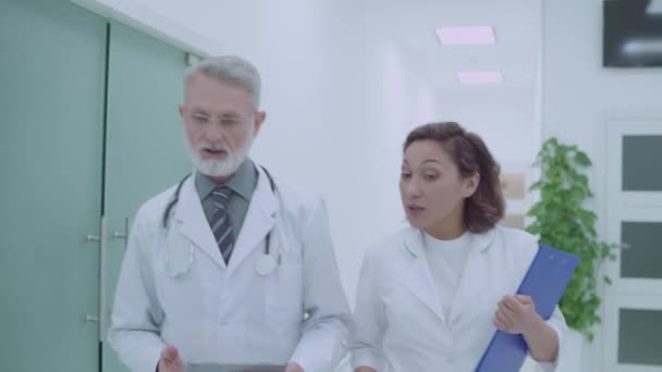 Profesyonel terapistler işi tartışıyor, klinik koridorunda yürüyorlar. — Stok video