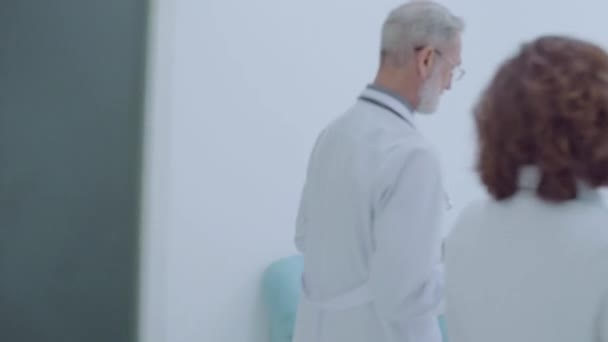 Médicos do sexo masculino e feminino discutem diagnóstico, caminhando juntos no hospital — Vídeo de Stock