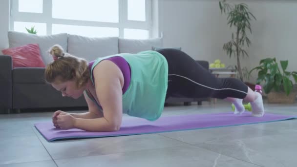 Hardwerkende mollig meisje doen plank oefening huis, training om overtollig gewicht te verliezen — Stockvideo