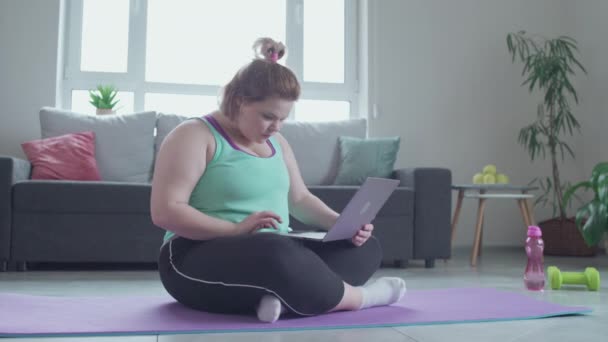 Избыточный вес женщины сидит на полу с ноутбуком, поиск полезных советов диеты — стоковое видео