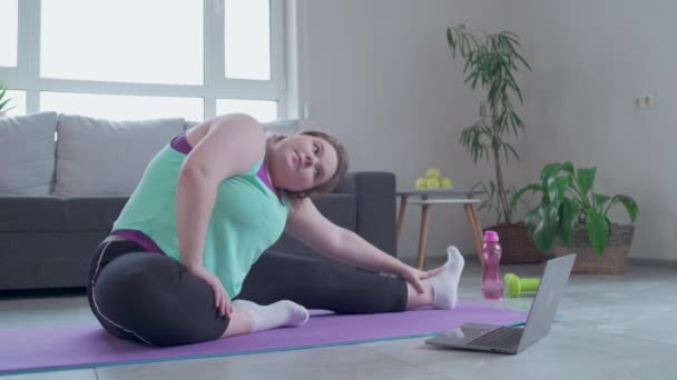 Плюс размер женщины, смотрящей фитнес видео урок на ноутбуке, упражнения на дому — стоковое видео