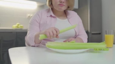 Mutsuz obez kadın kereviz çiğniyor, sebze diyetinden memnun değil, kilo kaybediyor.