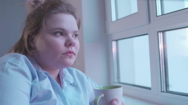 Pensive κορίτσι πίνοντας φλιτζάνι τσάι, κοιτάζοντας στο παράθυρο, ζεστή ατμόσφαιρα στο σπίτι — Αρχείο Βίντεο