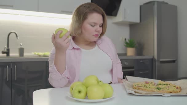 Пухленькая девушка выбирает между свежим яблоком и жирной нездоровой пищи, здоровый образ жизни — стоковое видео