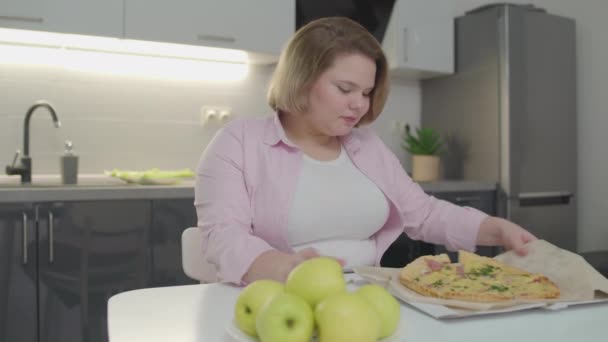 Plusz méretű lány választotta étvágygerjesztő pizza helyett friss alma, rossz akaraterő — Stock videók