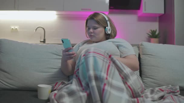 Plump female teenager in headphones listening to music, using smartphone app — Stock Video