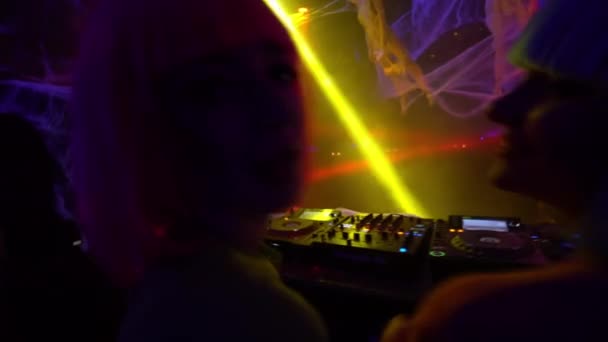 Two female disk jockeys in colorful wigs dancing to music in the night club, fun — Stock Video