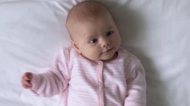 Yatakta uzanmış, merakla etrafa bakan tatlı yeni doğmuş bebek manzarası.