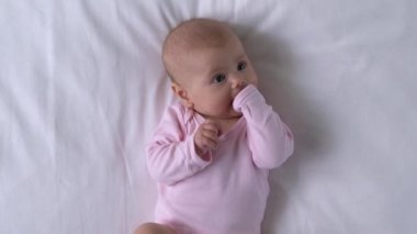 Minik ellerini ağzına koyup etrafa bakınan, neşeli bir bebek.