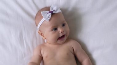 Sevimli bebek yatakta yatıyor, küçük kollarıyla hareket ediyor, etrafa bakıyor.