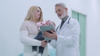 Genç anne ve aile doktoru tabletten randevu alıyor, klinikte konuşuyor.
