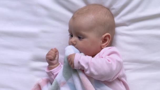Kaygısız bebek battaniye çiğniyor yatakta, diş çıkarma dönemi, erken çocukluk. — Stok video
