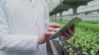 Erkek biyokimyacı tablette yazıyor, serada çalışıyor, biyolojik araştırmalar yapıyor.
