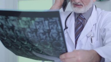 Erkek doktor telefonda konuşuyor, röntgen görüntüsü tutuyor, hastaya danışmanlık yapıyor, teşhis koyuyor.