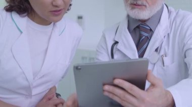 İki tıp uzmanı teşhisi tartışıyor, tablet resimlerine ve takım çalışmasına bakıyor.