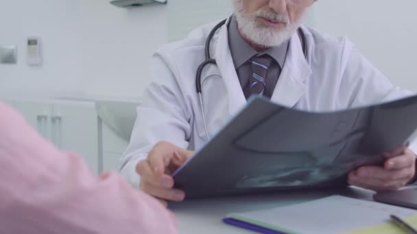 Хірург, який дивиться рентгенівське зображення, розмовляє з пацієнтом, консультація в лікарні — стокове відео