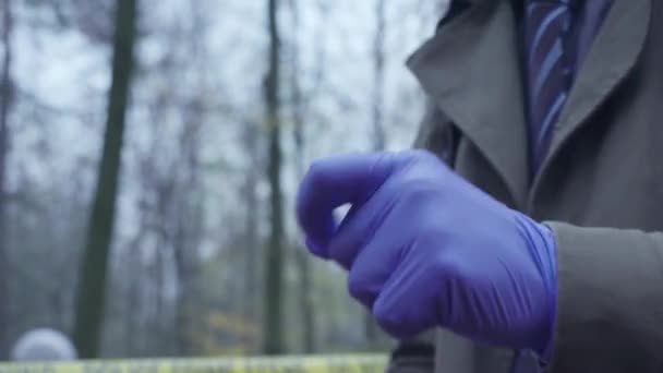 Следователь по уголовным делам надевает медицинские перчатки, входит на место преступления в лесу — стоковое видео