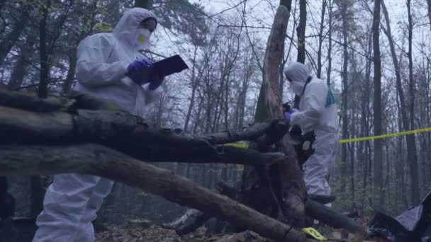 Dos peritos forenses examinando la escena del crimen en el bosque, recogiendo pruebas — Vídeo de stock