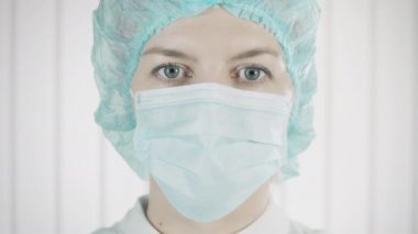 Koruyucu maskeli kadın doktor kameraya, sağlık çalışanına, mesleğine bakıyor.