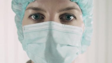 Koruyucu maskeli yorgun doktor kameraya bakıyor, aşırı çalışıyor, kendini feda ediyor.