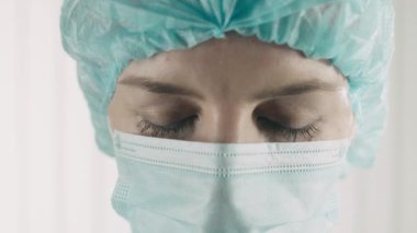 Koruyucu üniformalı ciddi bir kadın doktor kameraya bakıyor, evde kalmak istiyor.