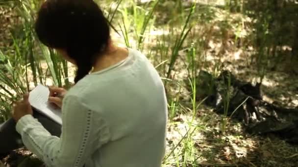 Fille écrit dans un cahier en forêt — Video