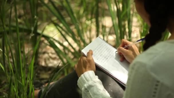 Flickan skriver i anteckningsboken i skogen — Stockvideo