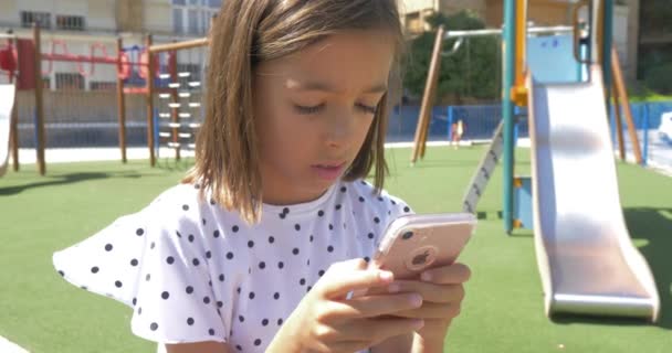 小可爱的漂亮女孩使用手机智能手机新技术在儿童游乐场 玩智能手机 — 图库视频影像