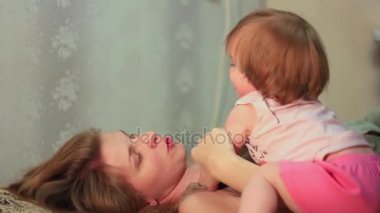 Anne yatakta bebekle oynuyor.