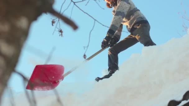 Человек убирает снег с крыши лопатой — стоковое видео